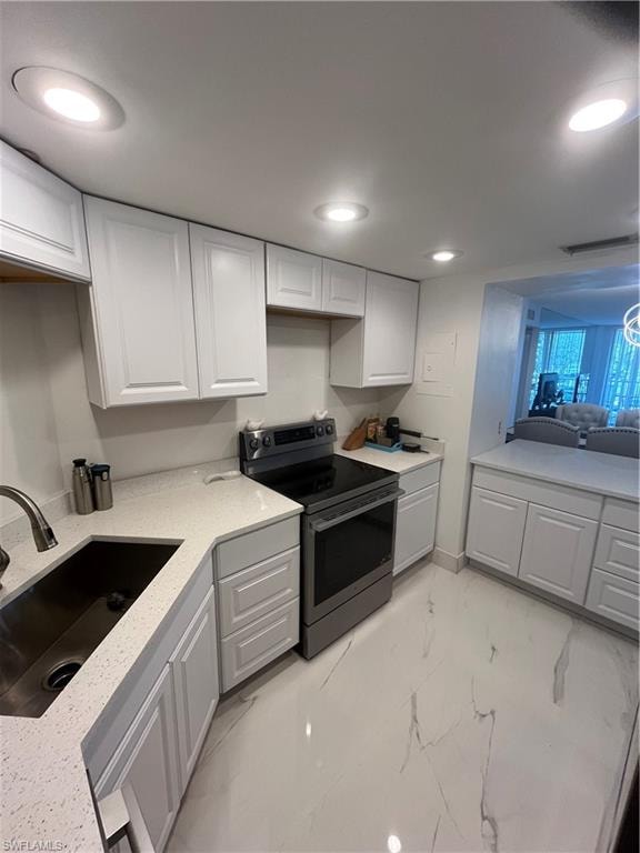 Kitchen featuring stainless steel range, white cabinets, recessed lighting, light stone counters, and light marble finish flooring