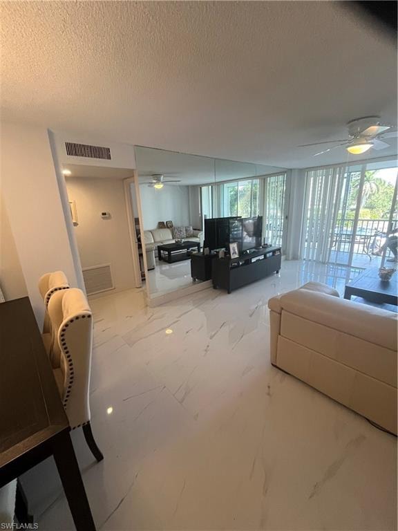 Living room with a ceiling fan, floor to ceiling windows, a textured ceiling, and light marble finish flooring