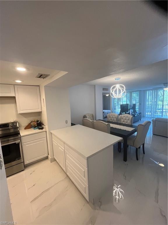 Kitchen with open floor plan, stove, white cabinetry, light countertops, and a peninsula