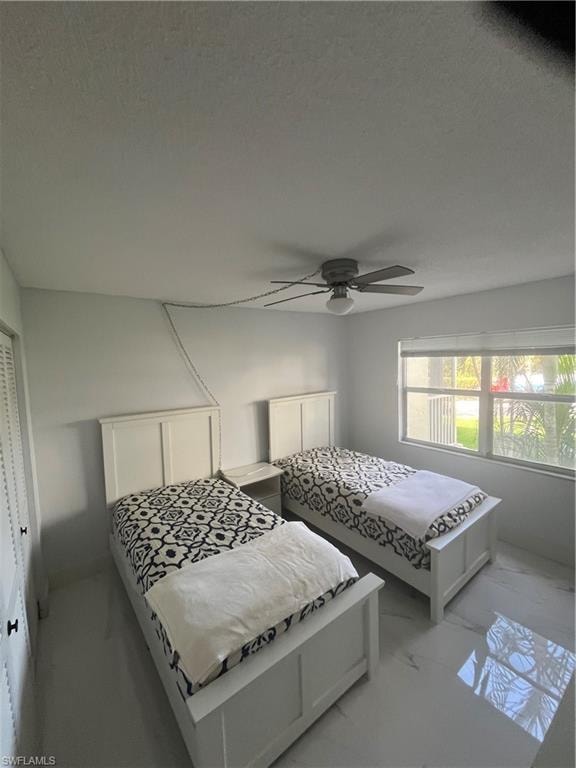 Bedroom with marble look tile flooring, a ceiling fan, and a closet