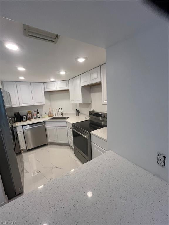 Kitchen with range, white cabinets, light marble finish floors, fridge, and recessed lighting