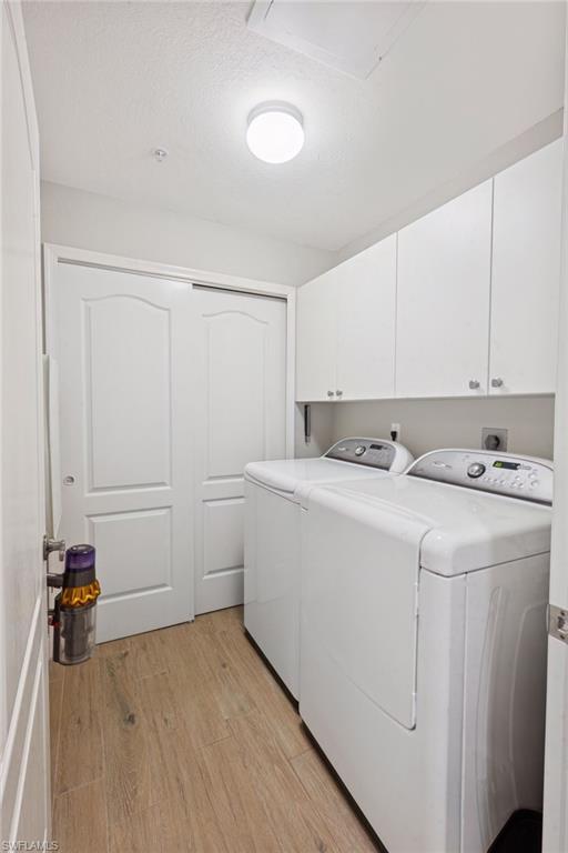 Laundry area with light wood-type flooring, independent washer and dryer, a textured ceiling, and cabinet space