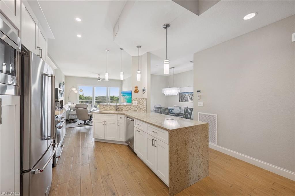 Kitchen featuring white cabinets, stainless steel appliances, light stone countertops, and light wood finished floors