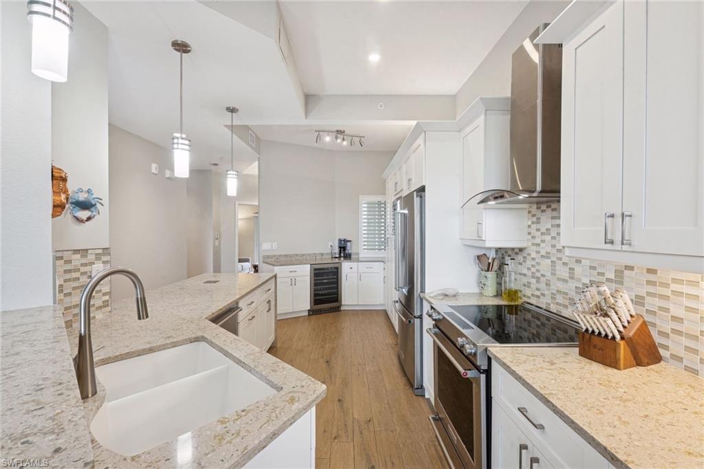 Kitchen featuring white cabinets, stainless steel appliances, wood floors, decorative backsplash, and light stone countertops