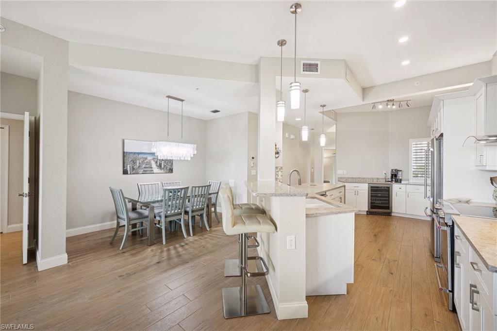 Kitchen with white cabinetry, a kitchen bar, hanging light fixtures, light wood floors, and light stone counters