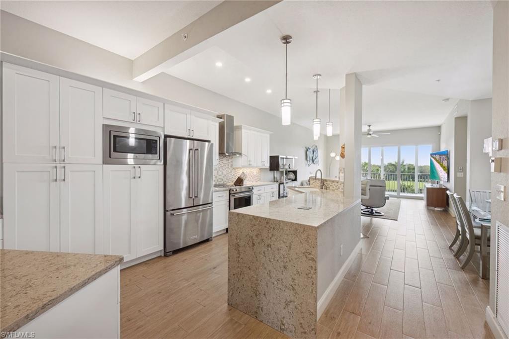 Kitchen featuring light stone countertops, stainless steel appliances, white cabinets, hanging light fixtures, and light wood-flooring