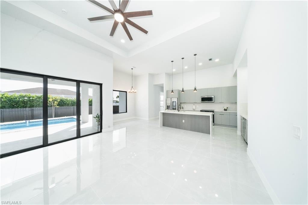 Kitchen with a center island with sink, a - raised ceiling, gray cabinets, decorative light fixtures, and a ceiling fan