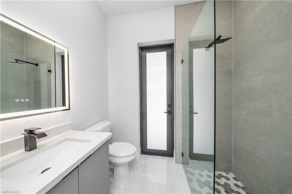 Full bath featuring vanity, a tile shower, and light tile patterned flooring