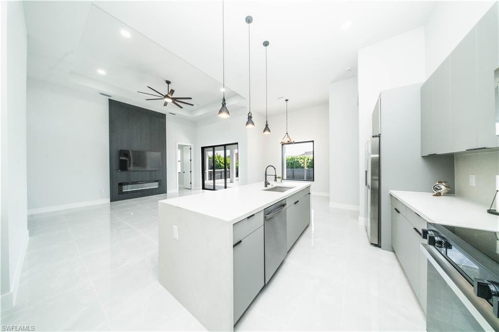 Kitchen with gray cabinetry, modernan cabinets, open floor plan, a center island with sink, and a raised ceiling