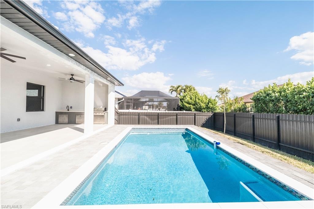 View of swimming pool with exterior kitchen, patio surround, and a fenced backyard