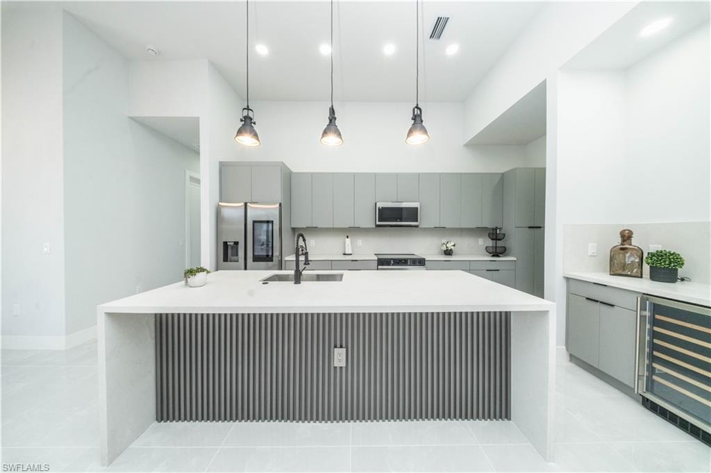 Kitchen featuring wine cooler, decorative light fixtures, gray cabinets, stainless steel appliances, and light stone counters