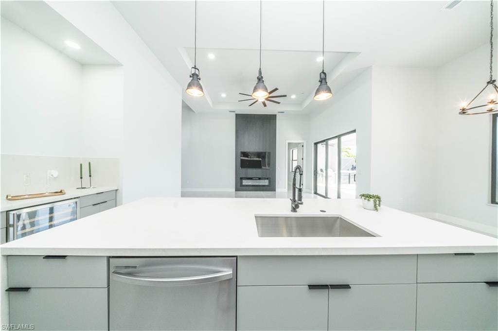 Kitchen featuring stainless steel l dishwasher, gray cabinetry, beverage cooler, pendant lighting, and a raised ceiling
