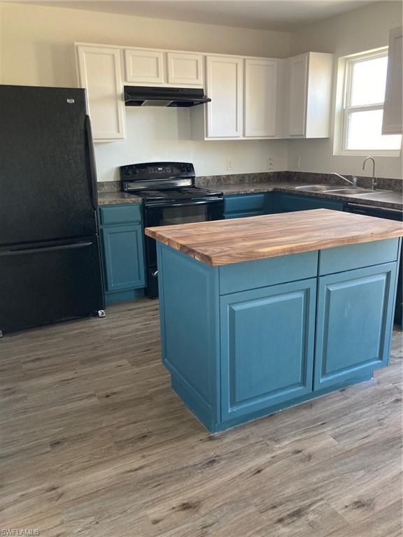 Two tone kitchen with butcher block countertops, refrigerator, two tone color scheme, black electric range, and a center island