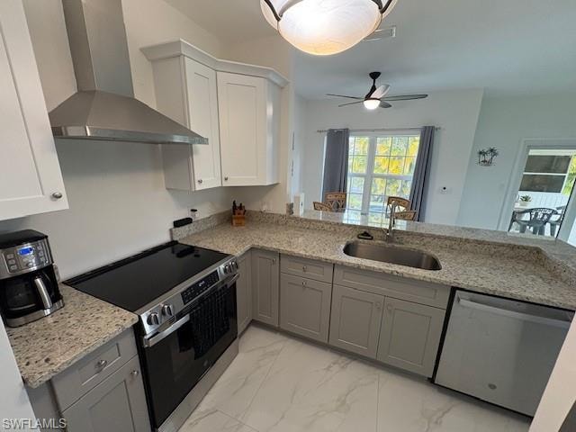 Two tone kitchen featuring stainless steel appliances, light stone counters, light marble finish floors, ceiling fan, and a peninsula