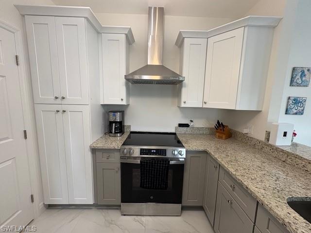 Kitchen featuring stainless steel range with electric cooktop, light stone counters, light marble finish floors, and two tone cabinetry