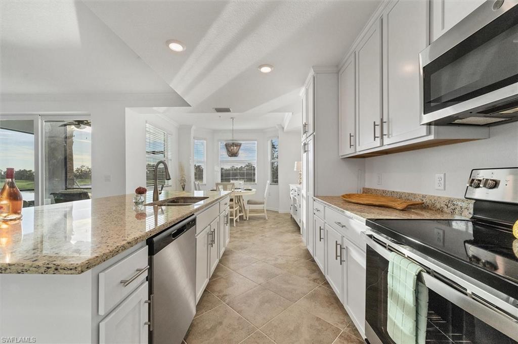Kitchen with stainless steel appliances, white cabinetry, an island with sink, light stone counters, and recessed lighting