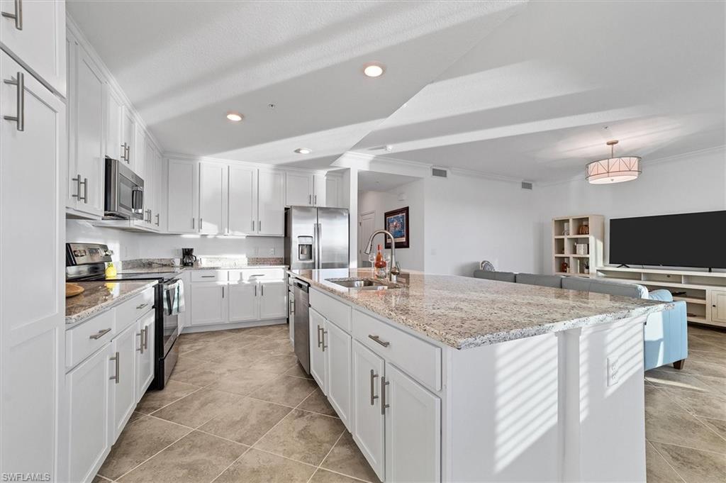 Kitchen featuring stainless steel appliances, light stone counters, a kitchen island with sink, white cabinetry, and recessed lighting