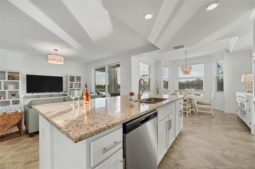 Kitchen with open floor plan, white cabinetry, stainless steel dishwasher, ornamental molding, and light stone counters