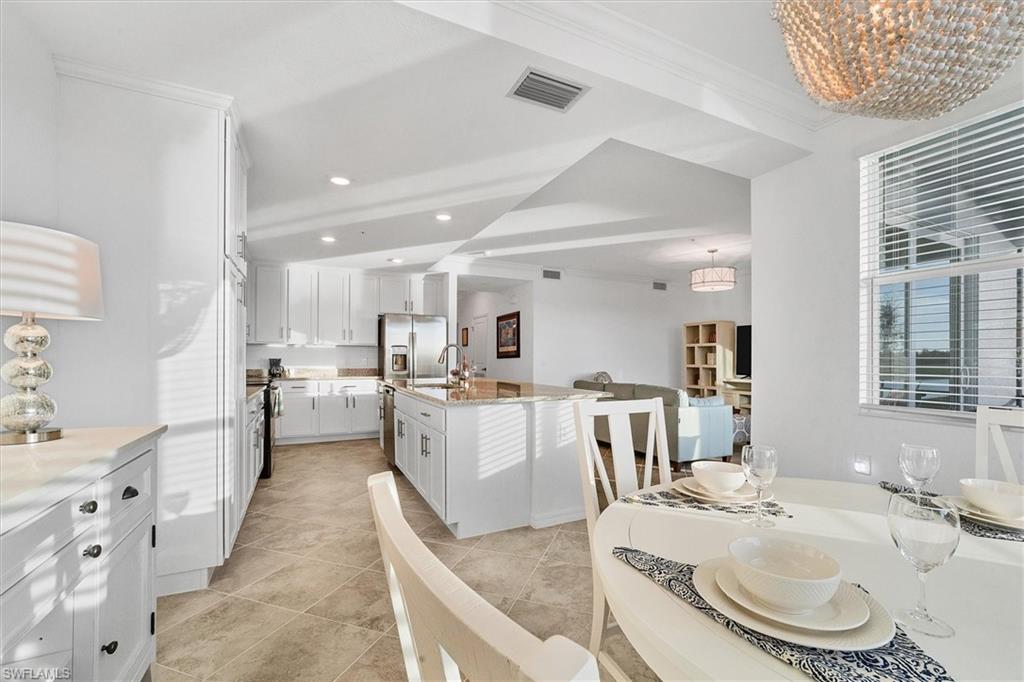 Kitchen with white cabinets, a center island with sink, light stone countertops, stainless steel refrigerator with ice dispenser, and open floor plan