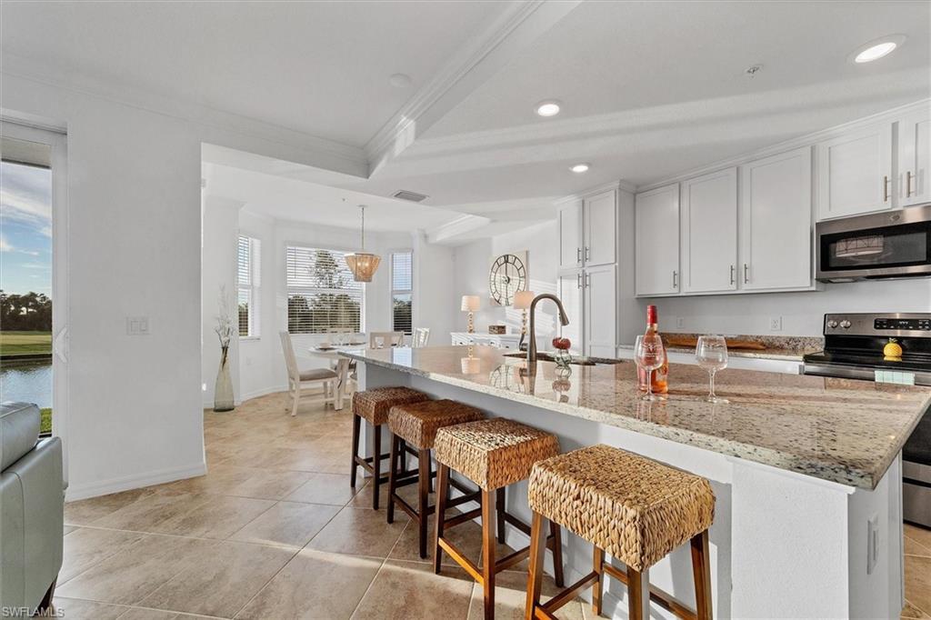 Kitchen featuring appliances with stainless steel finishes, a breakfast bar area, hanging light fixtures, light stone counters, and a center island with sink