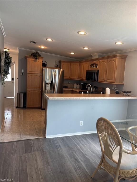 Kitchen featuring a peninsula, dark wood-type flooring, wood finish cabinets, crown molding, and recessed lighting