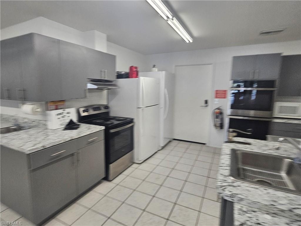 Kitchen with stainless steel appliances, gray cabinets, and light stone counters