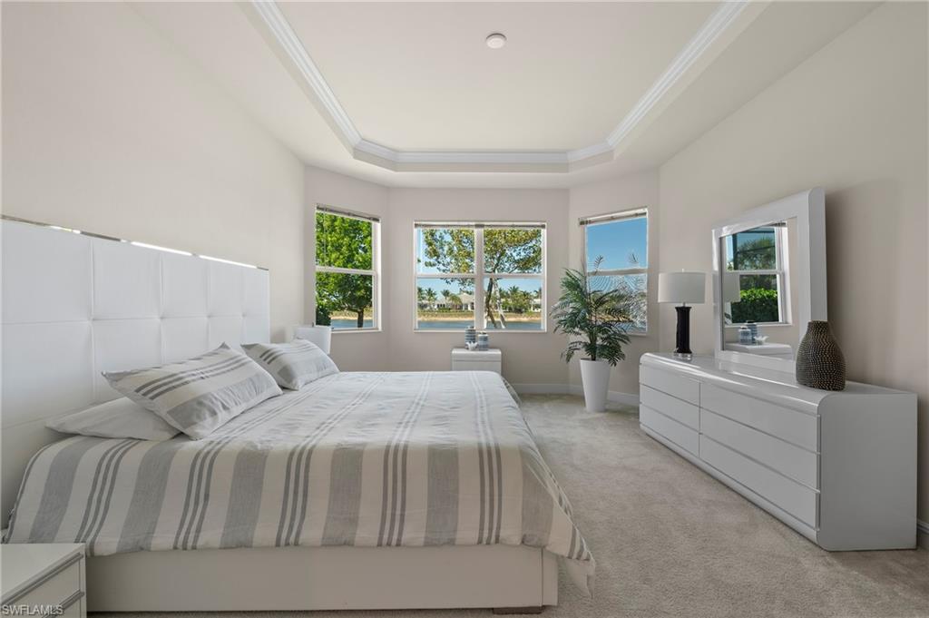 Bedroom with a raised ceiling, multiple windows, light colored carpet, and ornamental molding