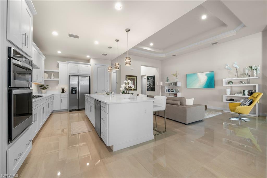 Kitchen featuring white cabinets, open floor plan, a breakfast bar area, decorative light fixtures, and stainless steel appliances