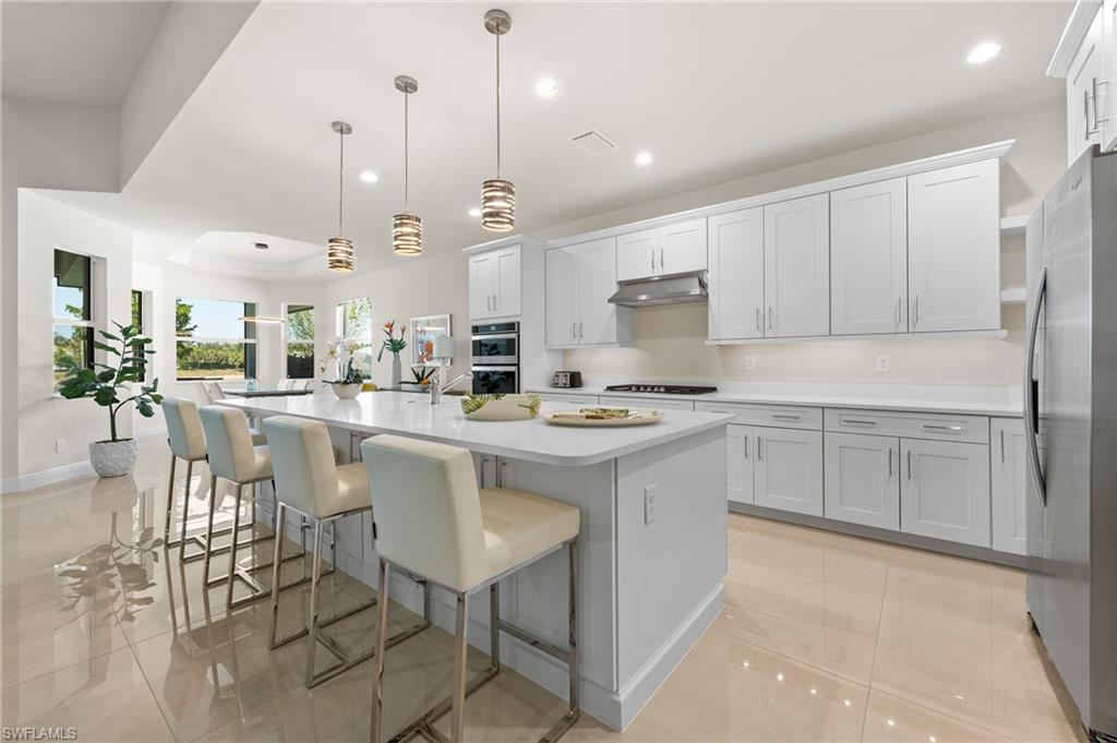 Kitchen featuring a kitchen island with sink, a kitchen breakfast bar, stainless steel appliances, decorative light fixtures, and white cabinetry