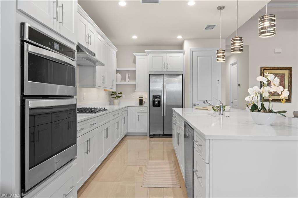 Kitchen with stainless steel appliances, white cabinets, a kitchen island with sink, open shelves, and hanging light fixtures