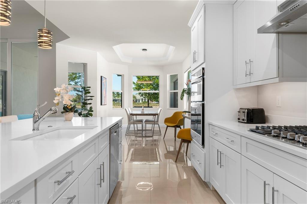 Kitchen featuring white cabinetry, hanging light fixtures, a raised ceiling, light stone counters, and stainless steel appliances