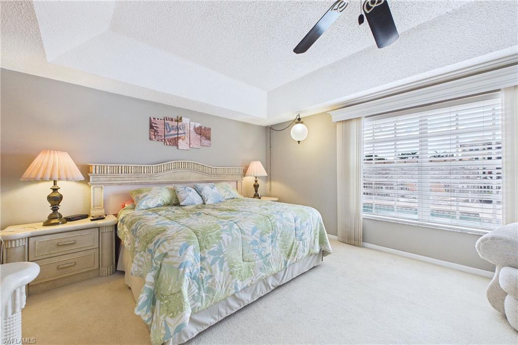 Bedroom featuring light carpet, a textured ceiling, a raised ceiling, and a ceiling fan
