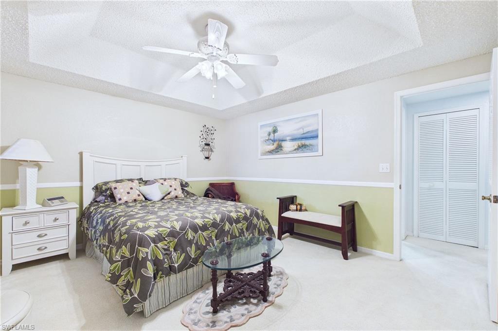Carpeted bedroom featuring a tray ceiling, a textured ceiling, and a ceiling fan