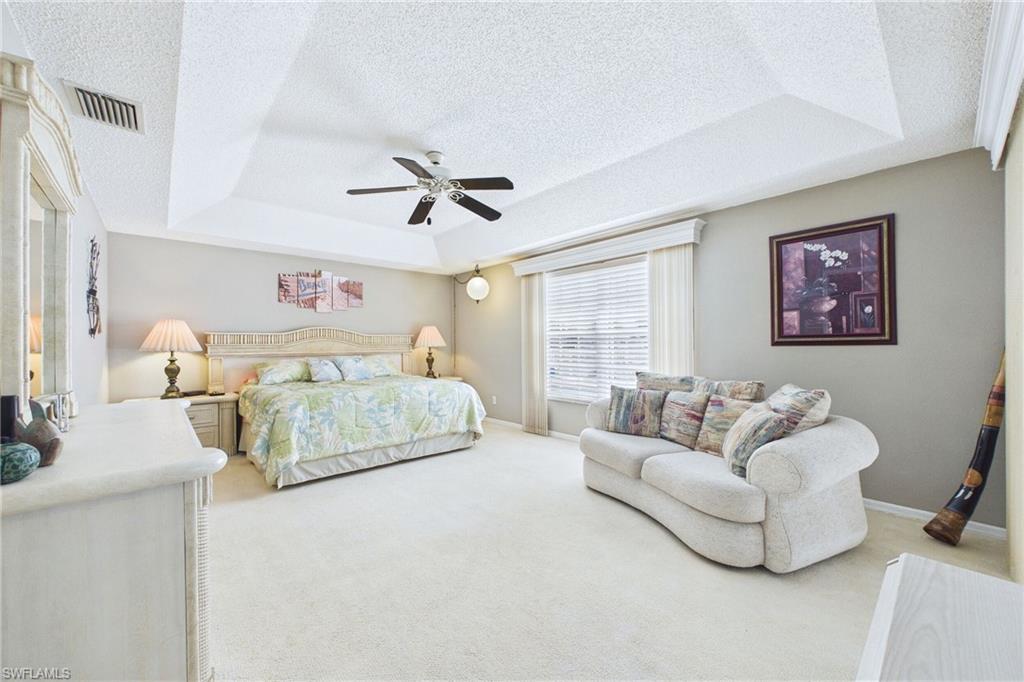 LARGE Primary Bedroom with a textured ceiling, a ceiling fan, light colored carpet, and a raised ceiling