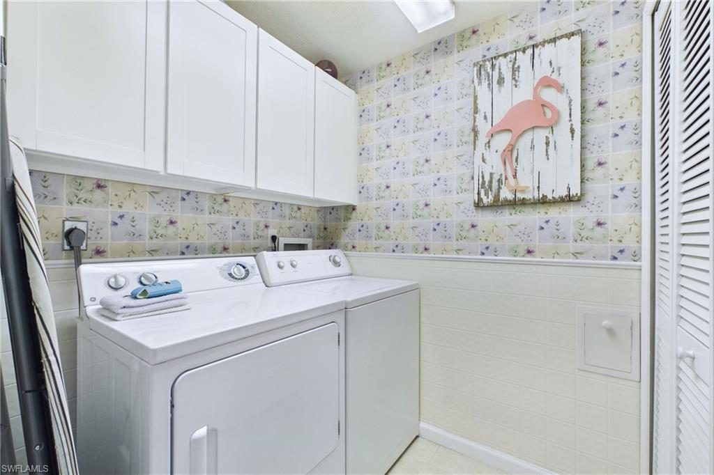 Laundry area featuring wallpapered walls, a wainscoted wall, tile walls, separate washer and dryer, and cabinet space