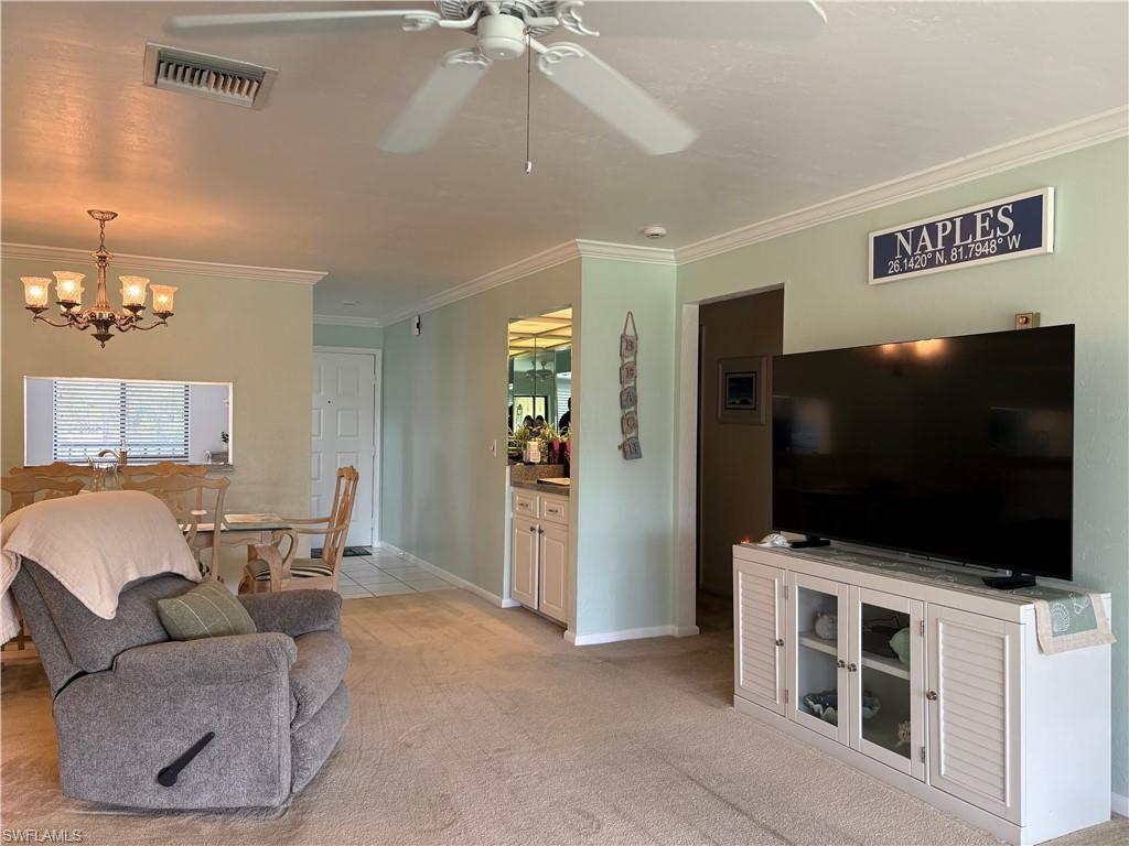 Living area featuring ornamental molding, light carpet, suspended lighting, and a ceiling fan
