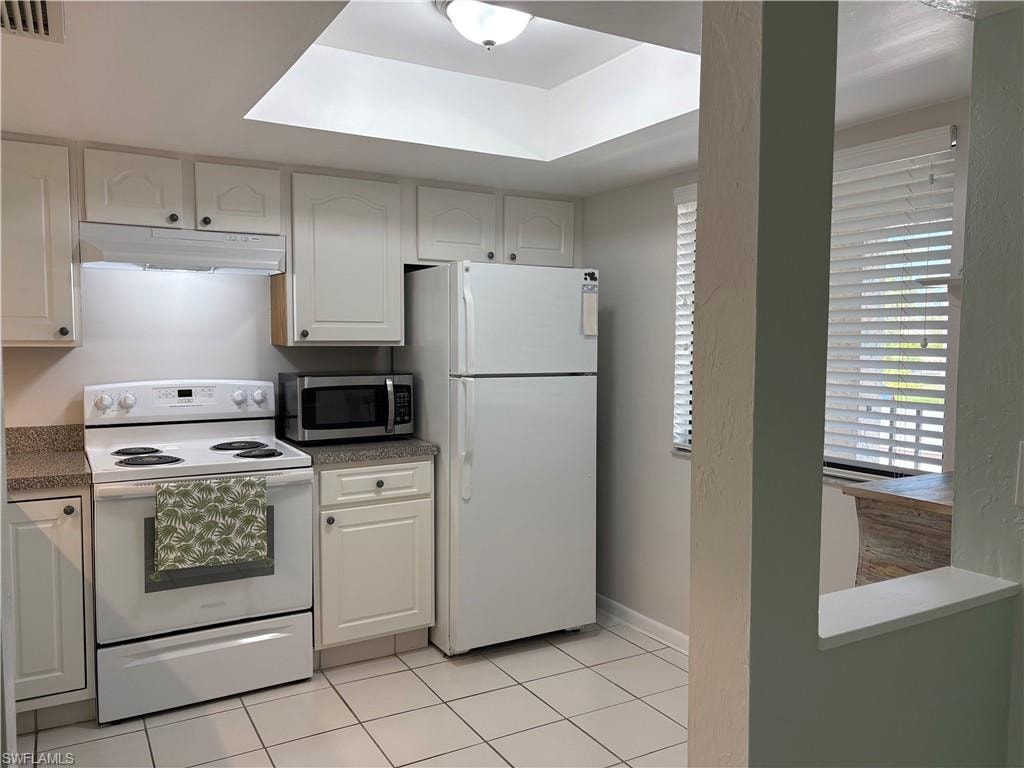 Kitchen featuring white appliances, light tile patterned floors, and white cabinetry
