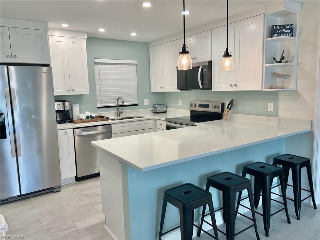 Kitchen featuring a breakfast bar, stainless steel appliances, a peninsula, and white cabinets