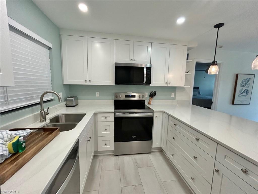 Kitchen with stainless steel appliances, white cabinets, pendant lighting, and light counters