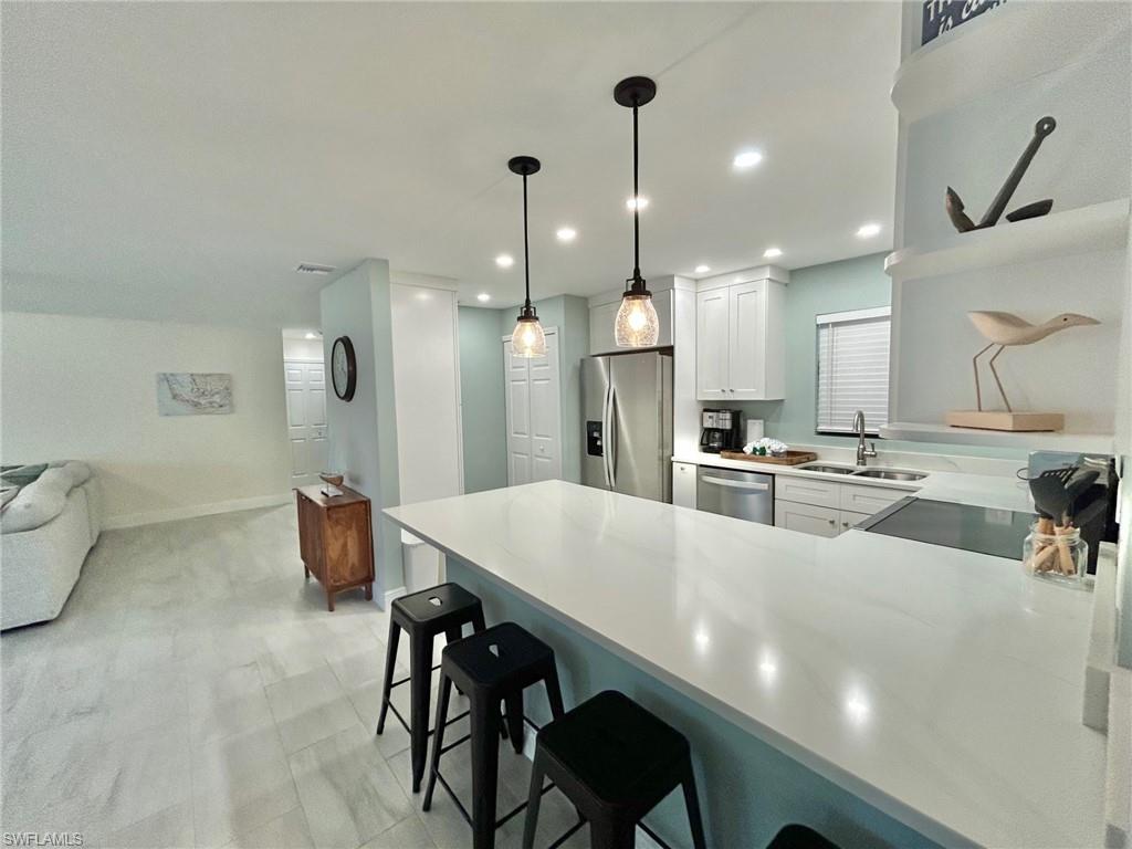 Kitchen featuring a kitchen breakfast bar, a peninsula, stainless steel appliances, white cabinetry, and hanging light fixtures