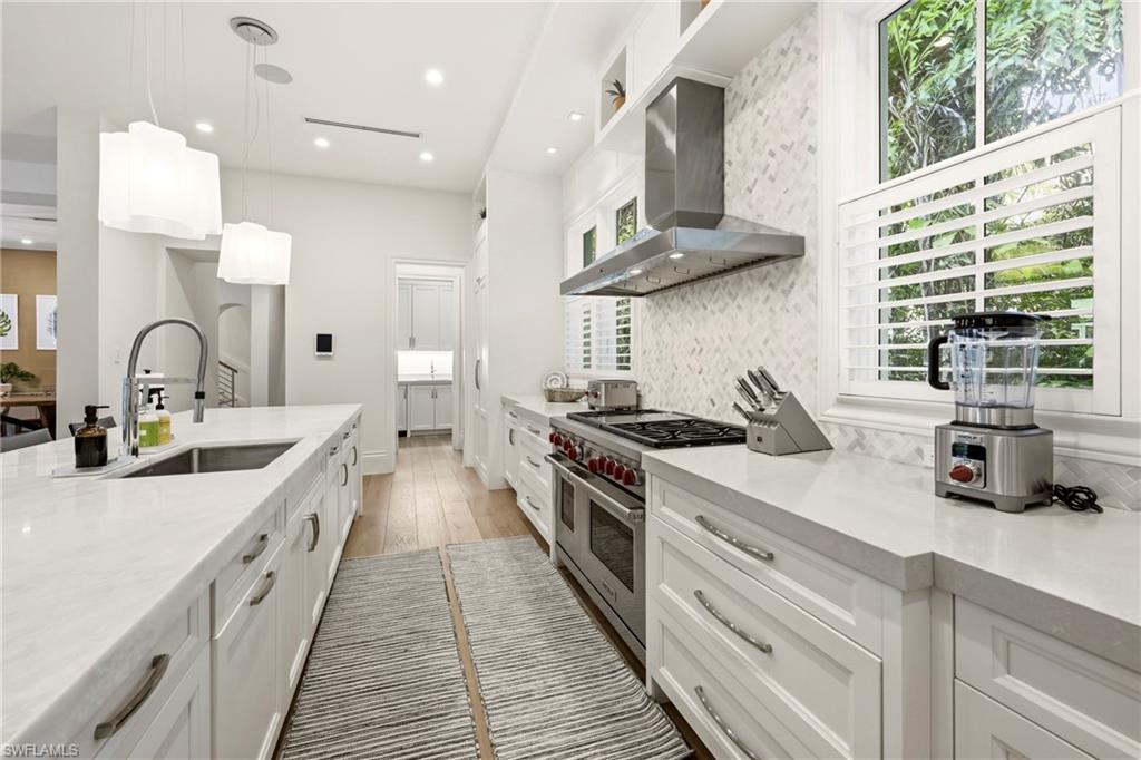 Kitchen featuring light stone counters, white cabinetry, decorative light fixtures, double oven range, and light wood finished floors