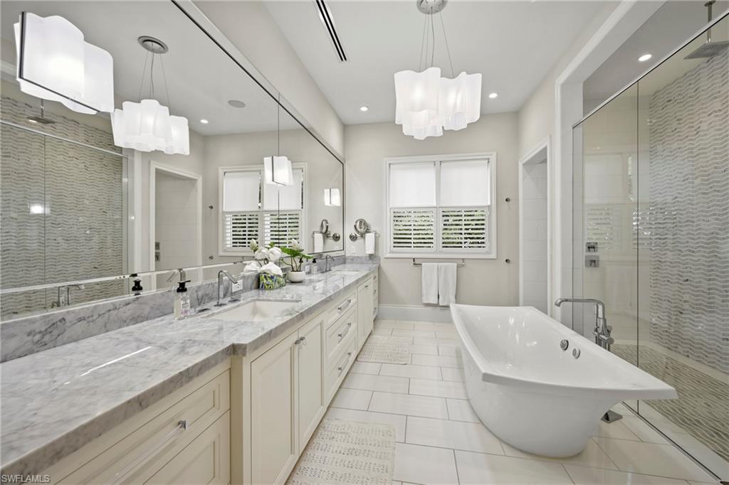Full bathroom with a shower stall, double vanity, light tile patterned flooring, a freestanding tub, and suspended lighting