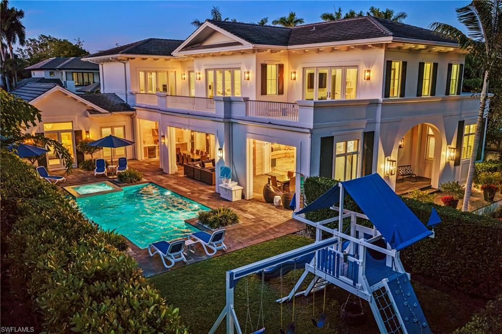 Back of house at dusk featuring a balcony, a patio, stucco siding, a tile roof, and a pool with connected hot tub