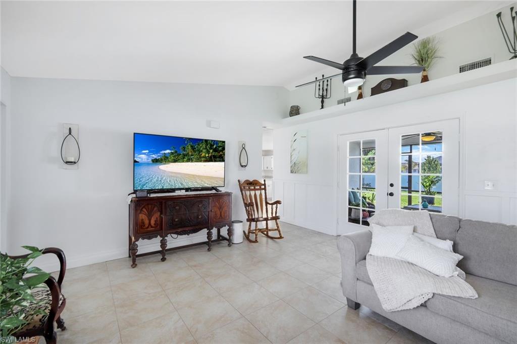 Living room with lofted ceiling, a ceiling fan, light tile patterned flooring, french doors, and a decorative wall