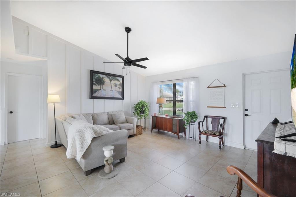 Living area featuring vaulted ceiling, ceiling fan, light tile patterned floors, and a decorative wall