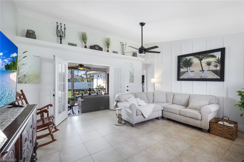 Living area with a decorative wall, french doors, ceiling fan, light tile patterned flooring, and a high ceiling