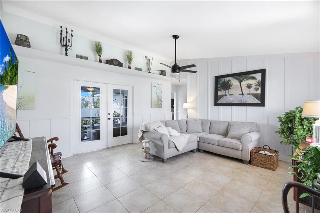 Living area featuring a decorative wall, french doors, a ceiling fan, and light tile patterned floors