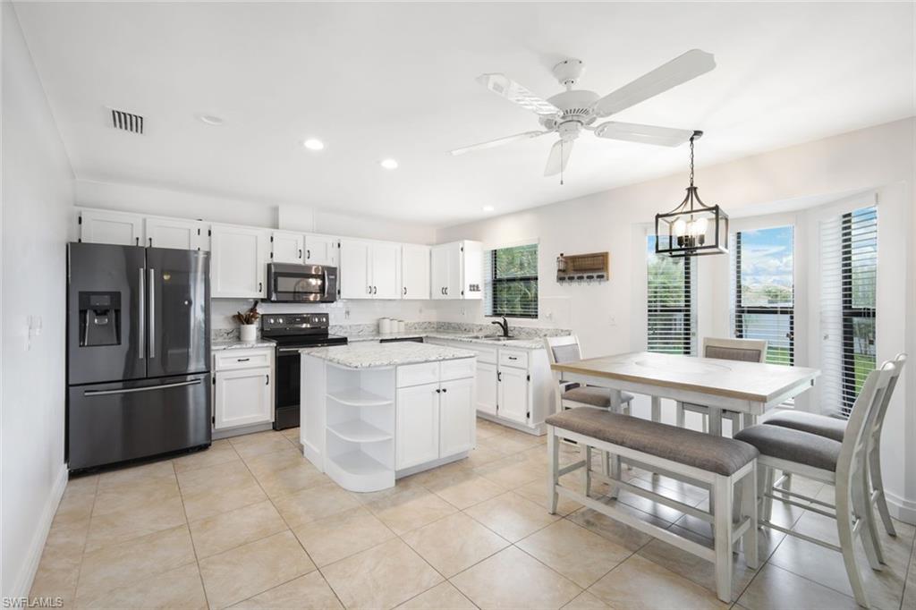 Kitchen featuring stainless steel appliances, white cabinetry, light stone counters, a center island, and a ceiling fan