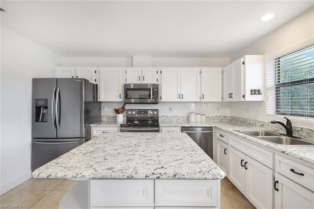Kitchen with white cabinetry, stainless steel appliances, a kitchen island, light stone counters, and light tile patterned floors