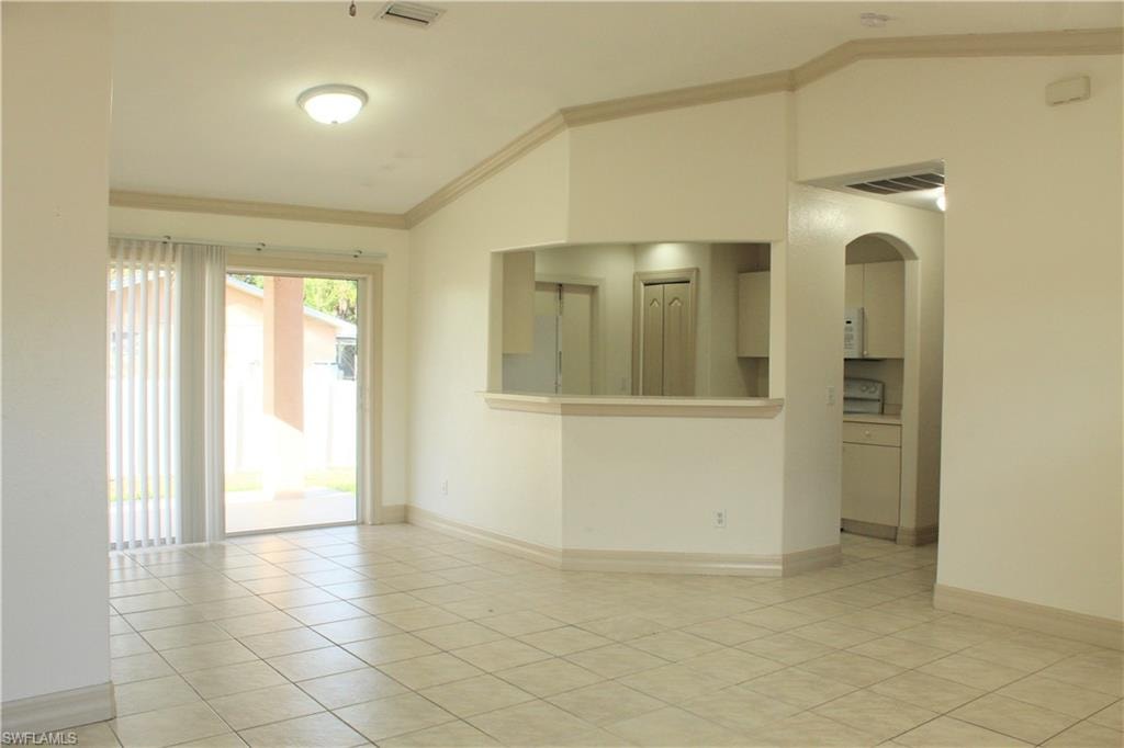 Unfurnished room featuring lofted ceiling, crown molding, arched walkways, and light tile patterned floors